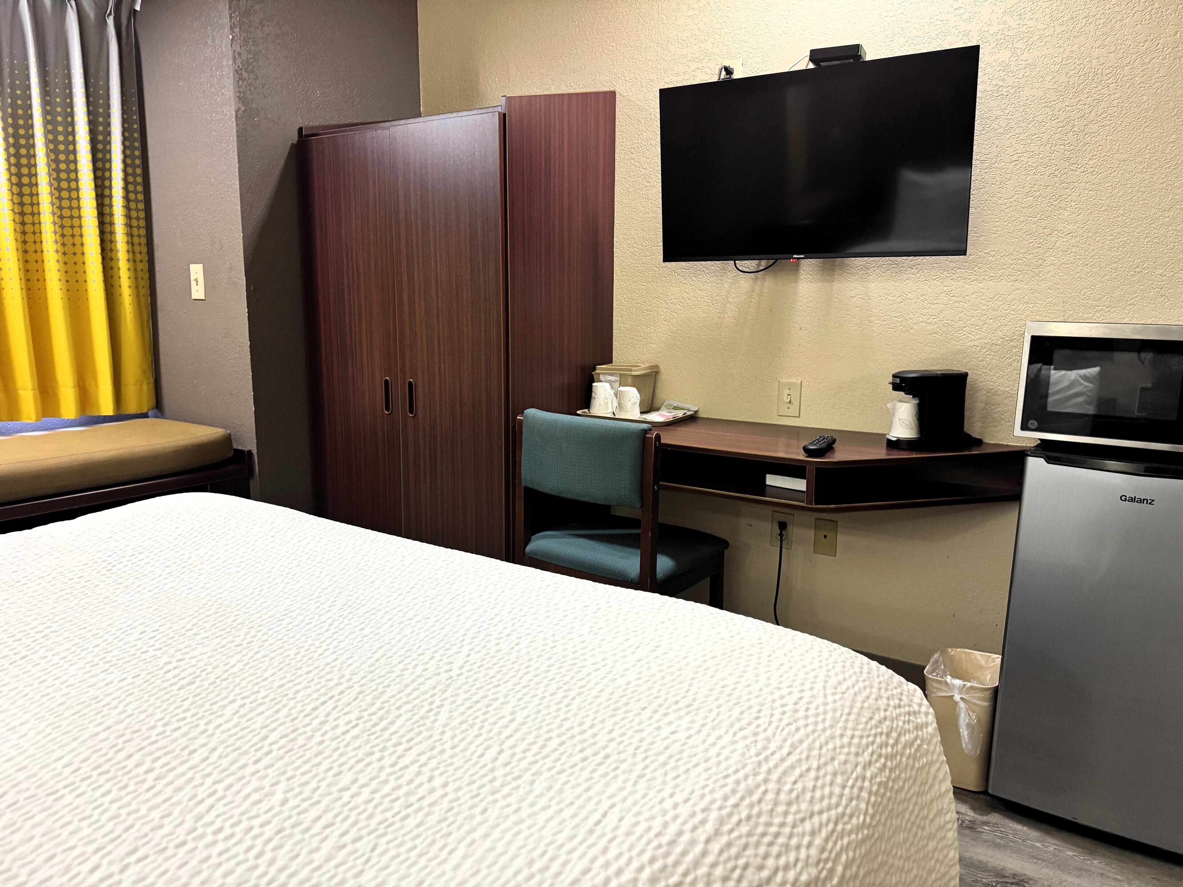 A hotel room with a bed, a desk with a chair, a television, a coffee maker, and a refrigerator.
