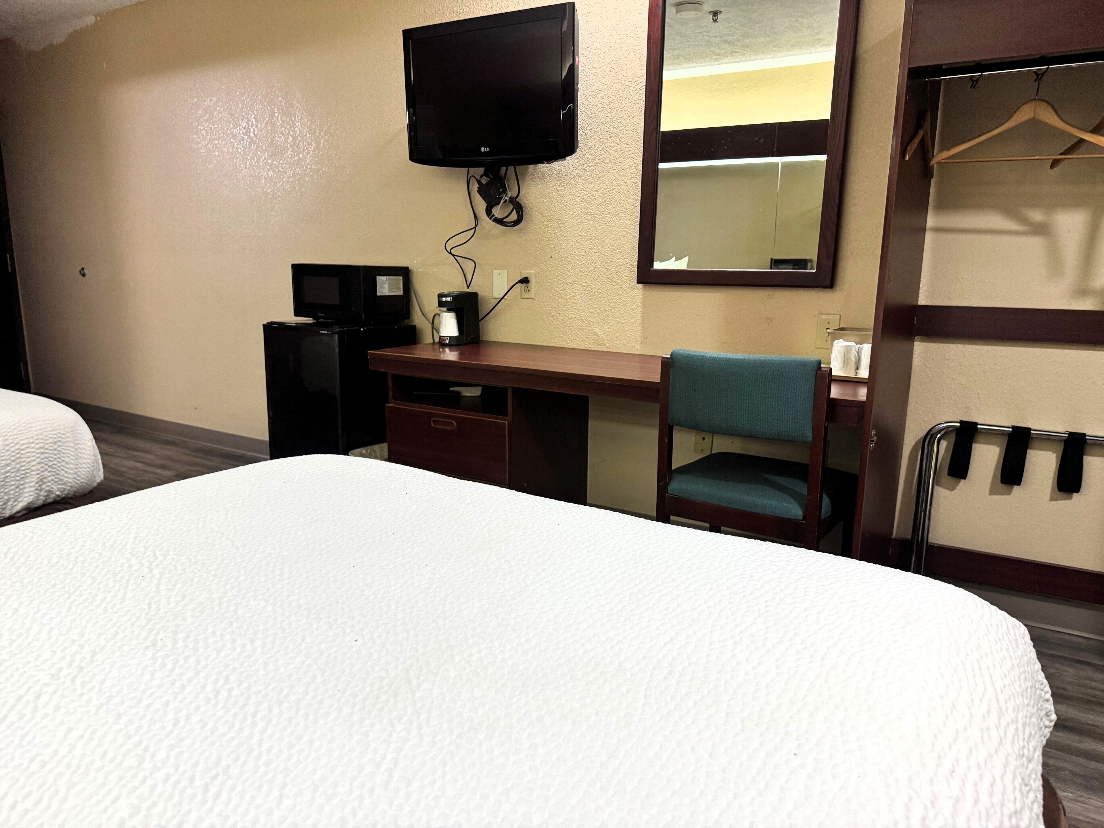 A hotel room with a bed, a desk with a chair, a television, and a mirror.