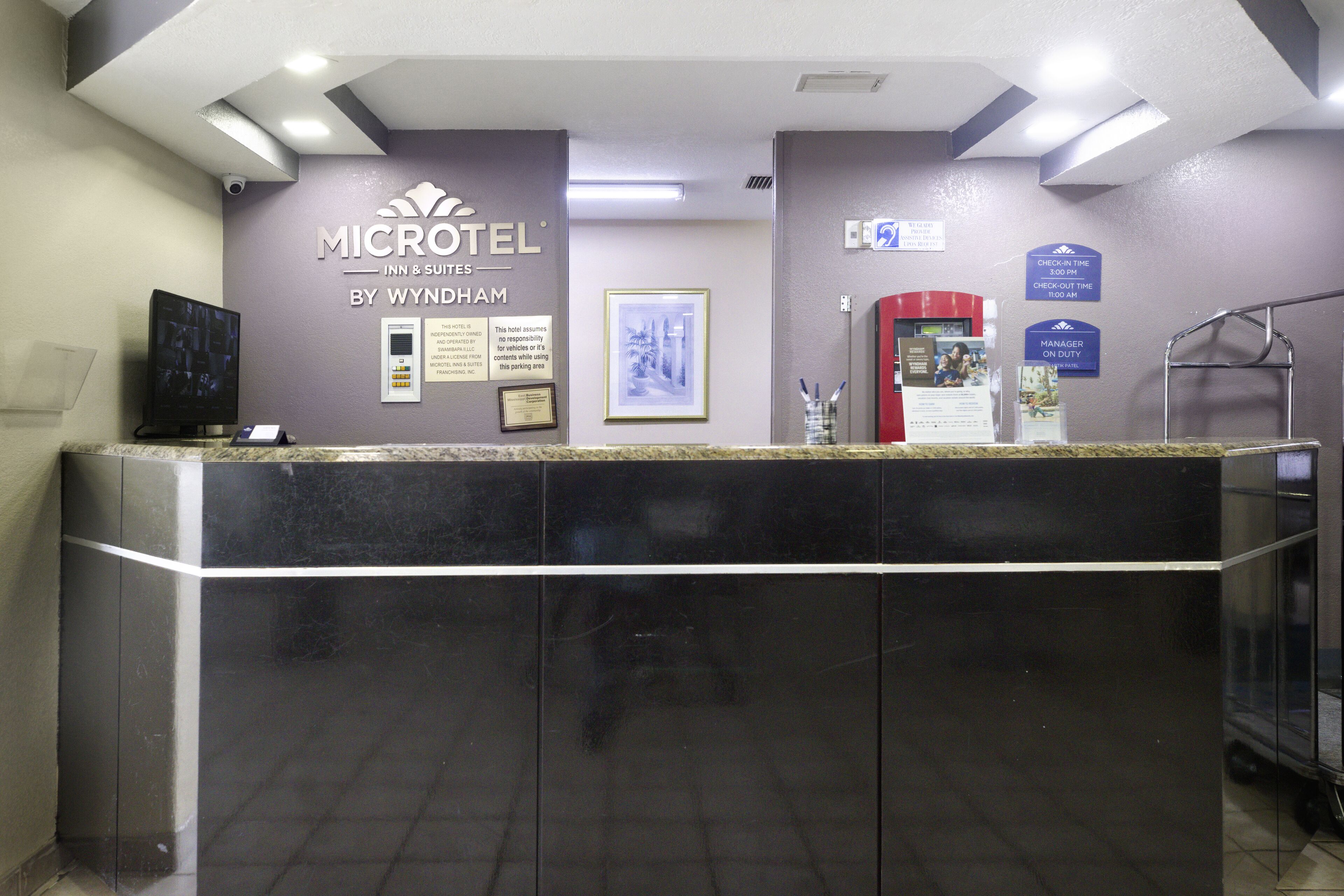 A reception desk at a Microtel Inn & Suites by Wyndham with a check-in counter, a framed photo, and informational signs.