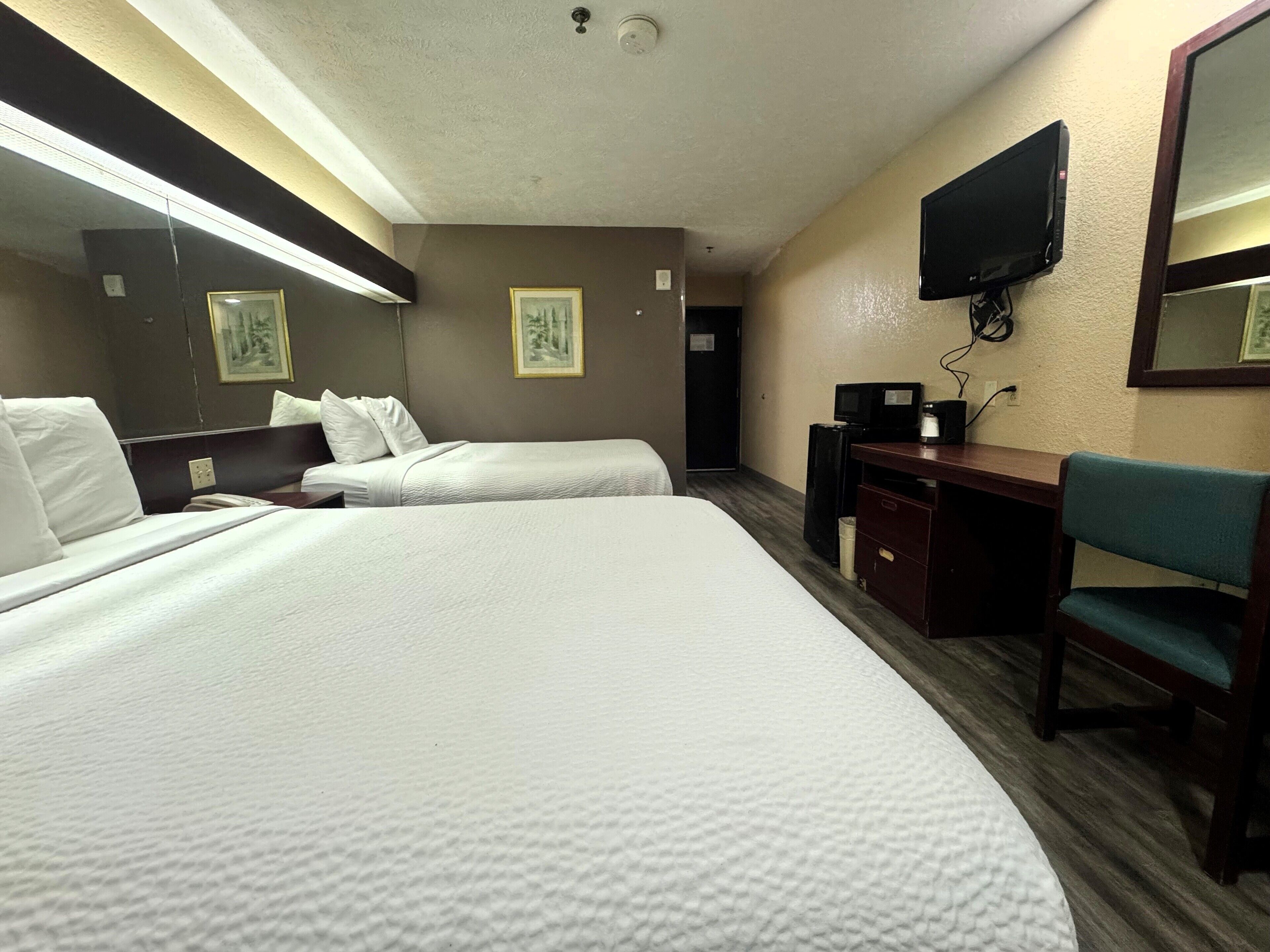 Quarto de hotel com duas camas, uma escrivaninha, uma cadeira, televisão e quadros nas paredes.