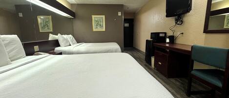 A hotel room with two beds, a desk, a chair, a television, and framed pictures on the walls.