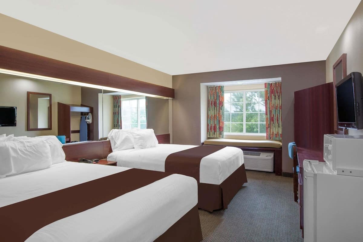 Habitación de hotel con dos camas, televisión, escritorio y ventana con cortinas.