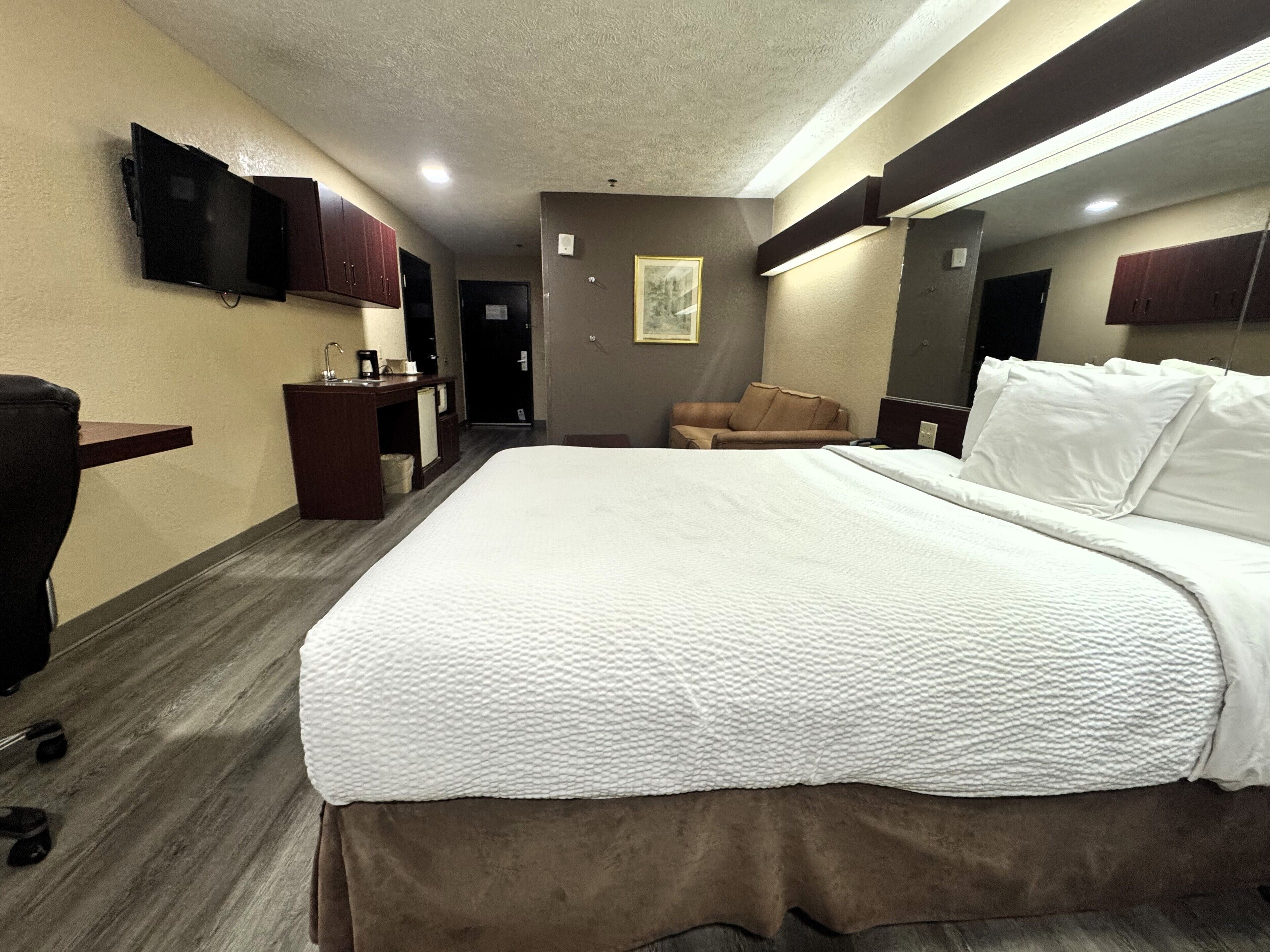 A hotel room with a large bed, a desk with a chair, a television, and a mirror.