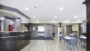 A clean, modern indoor space with a reception desk, a self-service kiosk, and several tables and chairs arranged for dining. - Microtel Inn & Suites by Wyndham Meridian (Meridian)