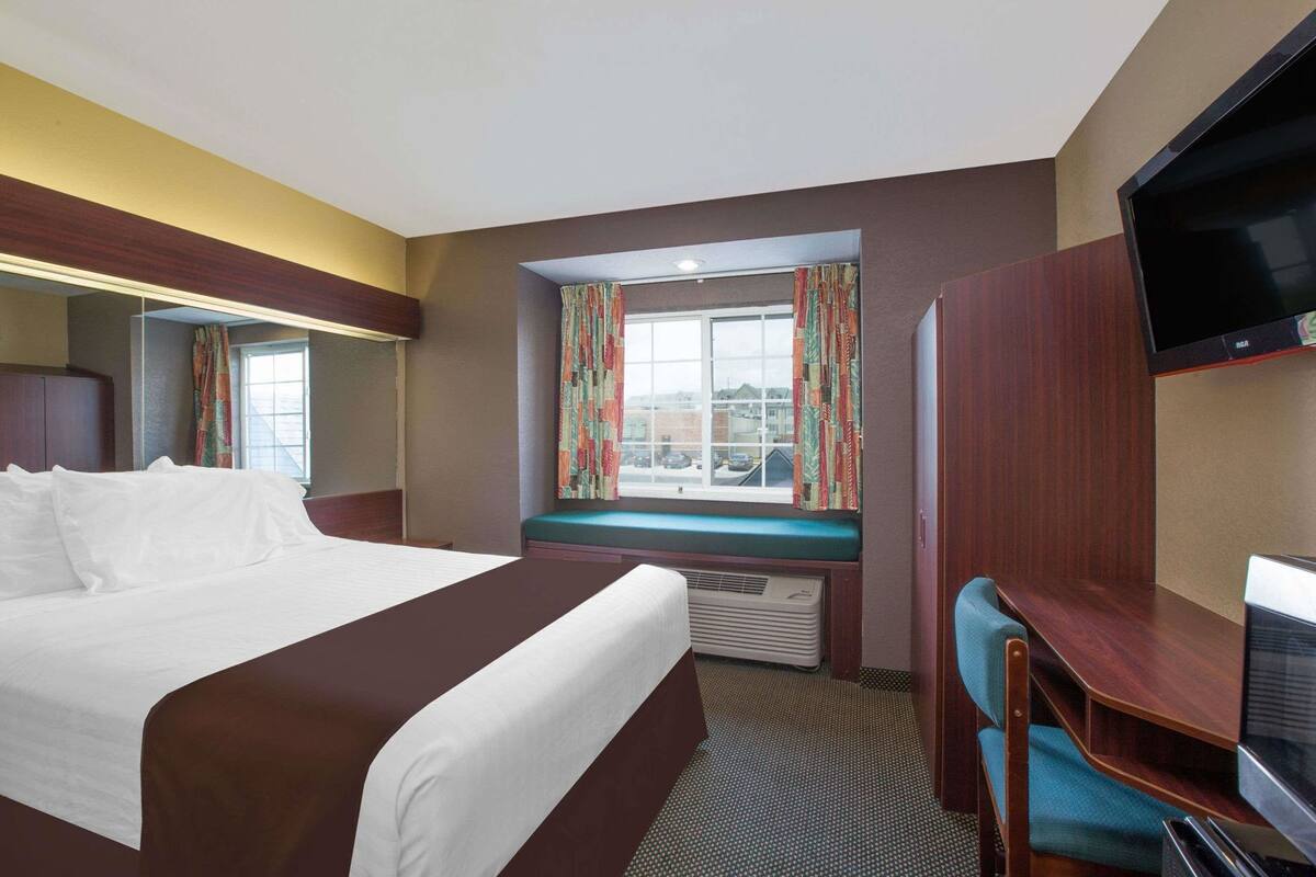 Habitación de hotel con cama, escritorio, televisor, ventana con cortinas y vistas al exterior.