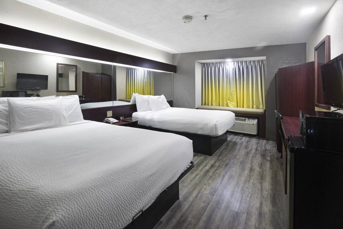 A hotel room with two beds, a TV, a desk, and a window with curtains.