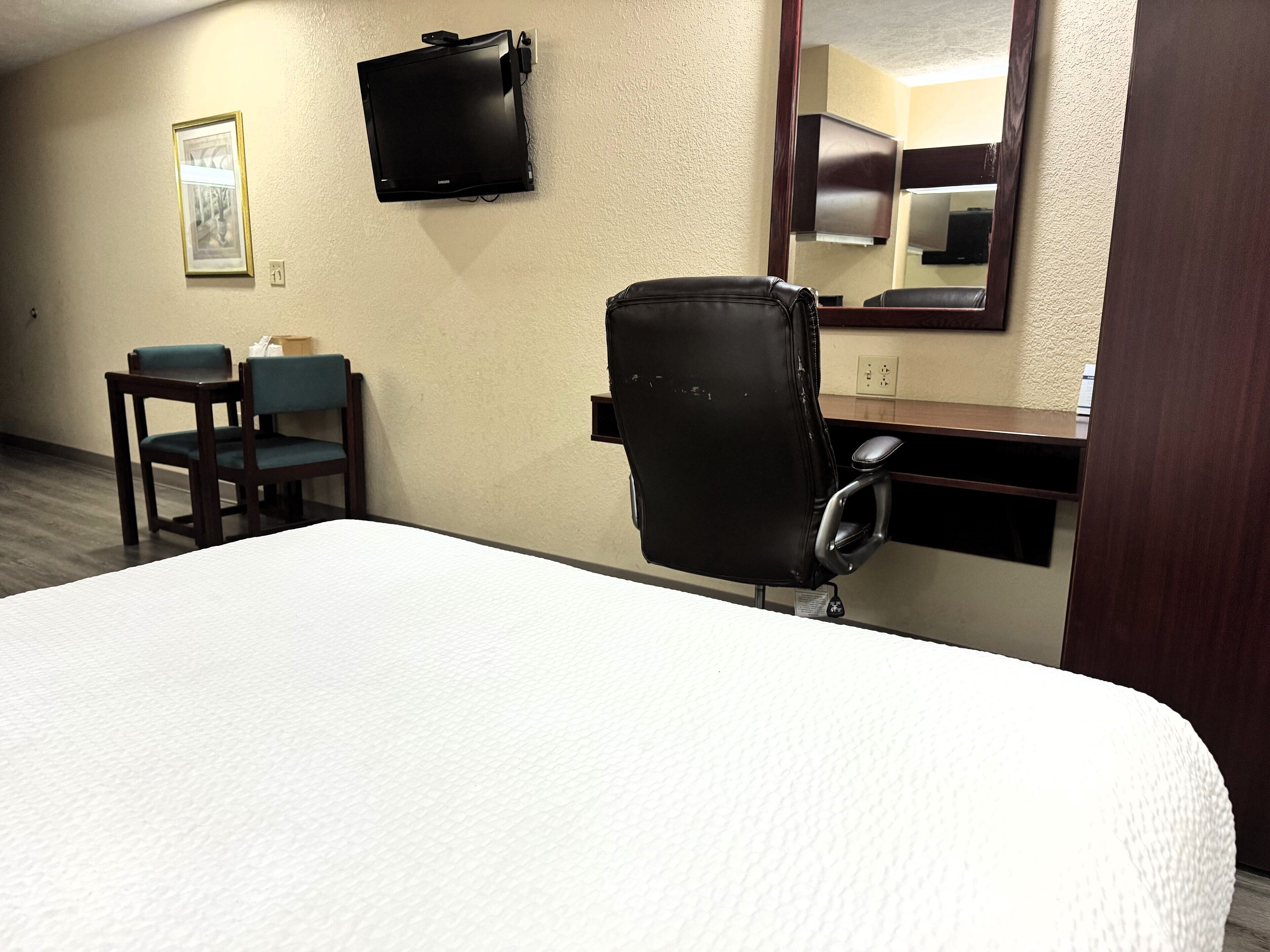 A hotel room with a bed, a desk, a chair, a television, and a mirror.