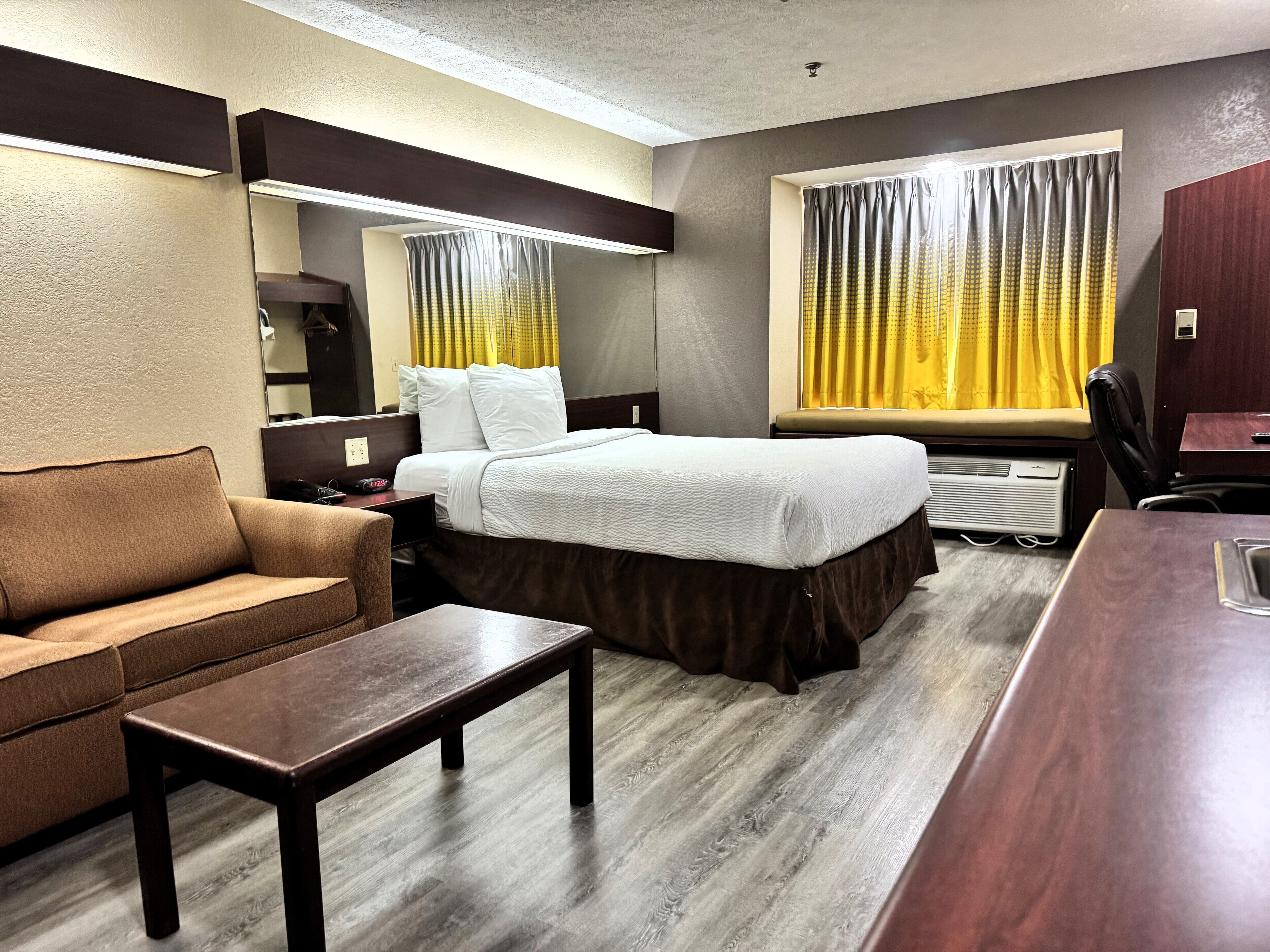 Een hotelkamer met een bed, een slaapbank, een bureau en een raam met gordijnen.