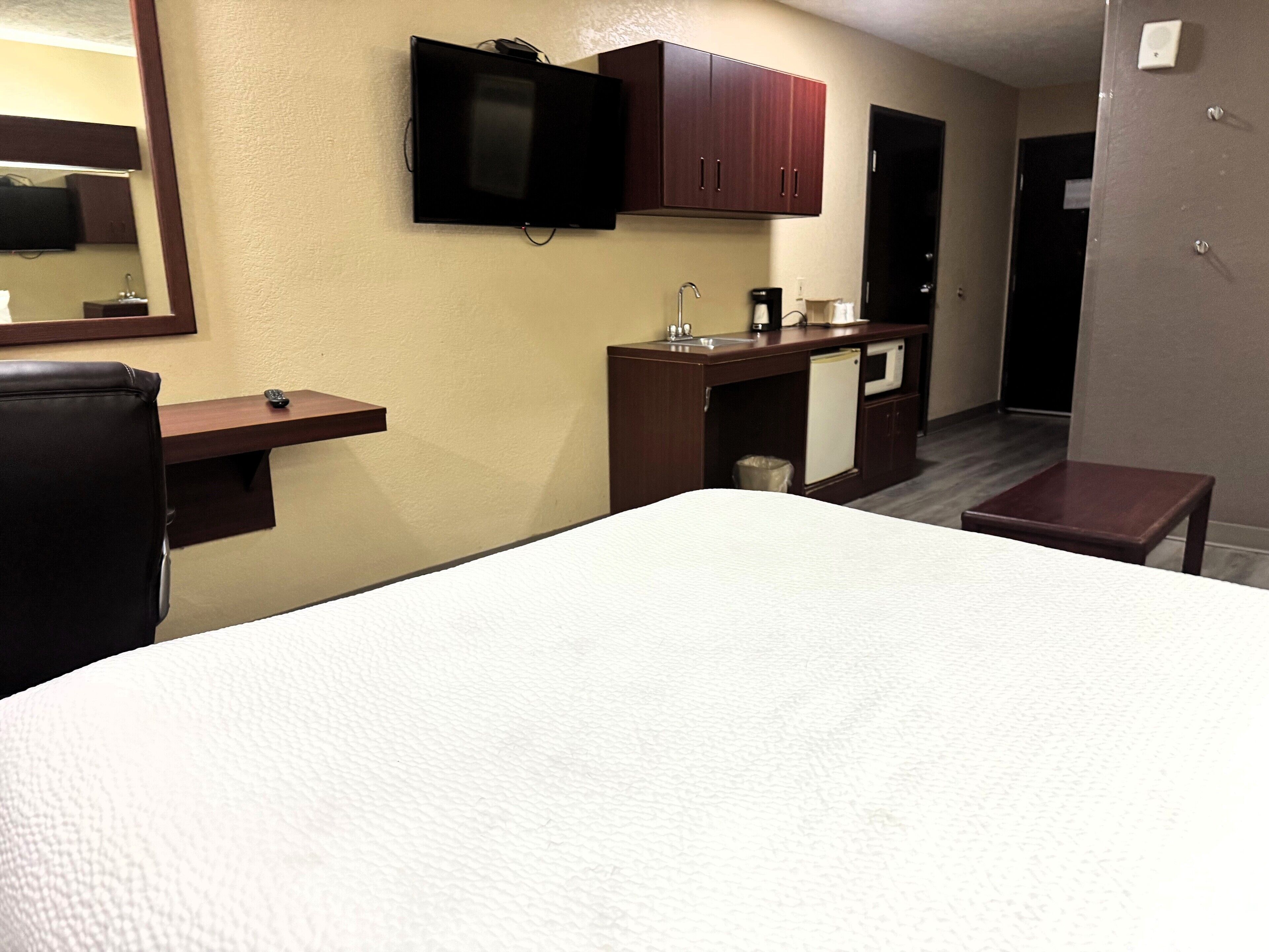 A hotel room with a bed, a desk, a television, a minibar, and a small table.