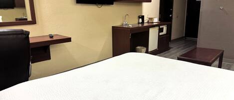 A hotel room with a bed, a desk, a television, a minibar, and a small table.