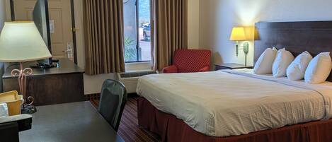 A hotel room with a bed, desk, chair, and a window with curtains.