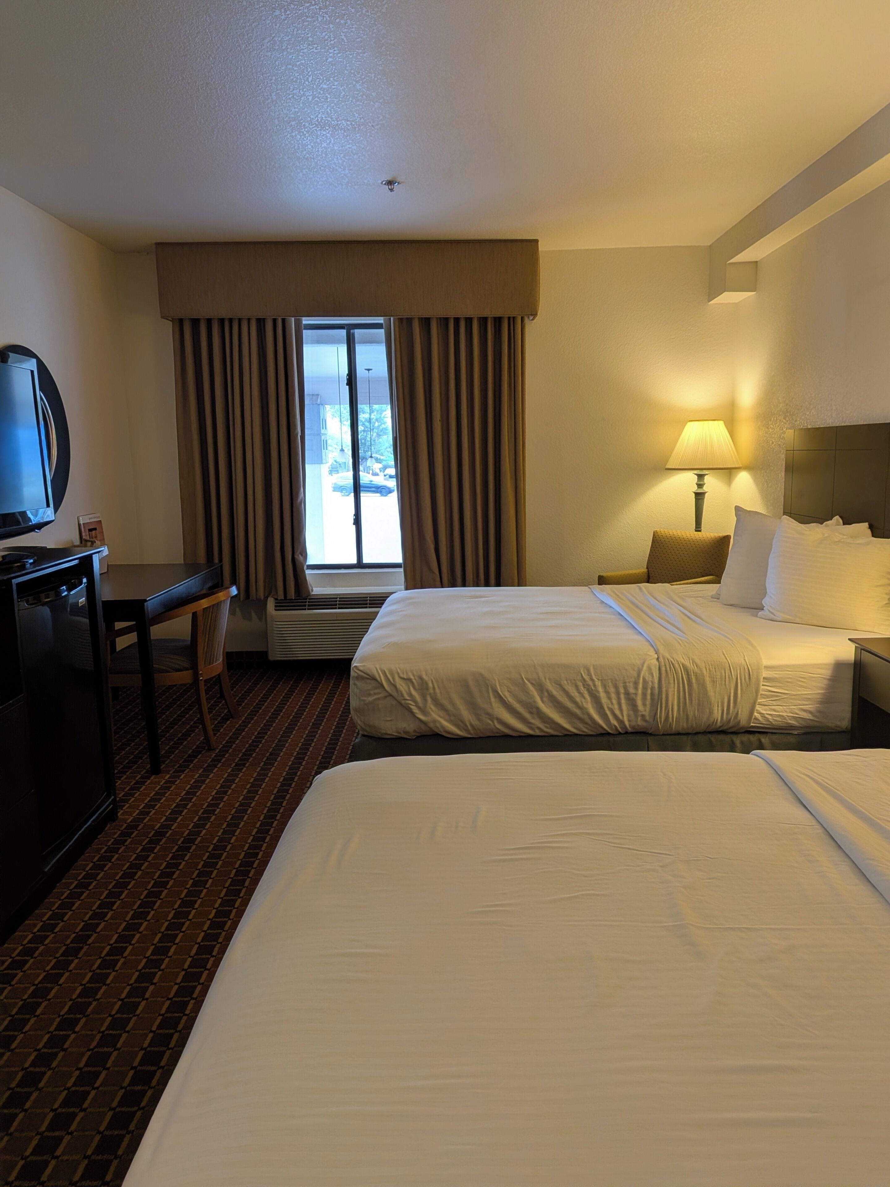 Une chambre d’hôtel avec deux lits, un bureau, une télévision et une fenêtre avec des rideaux.