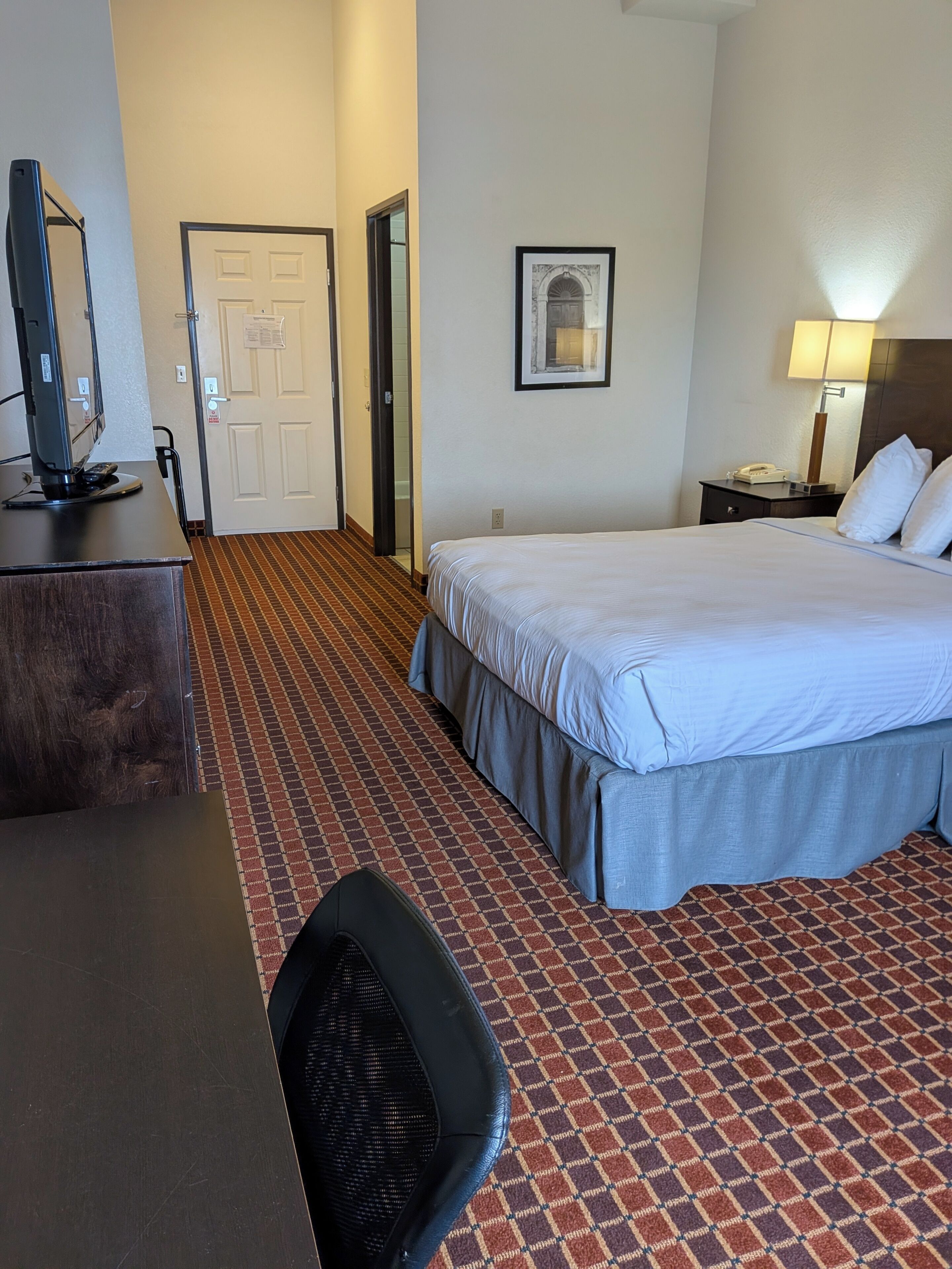 A hotel room with a bed, desk, chair, and a door leading to a bathroom.