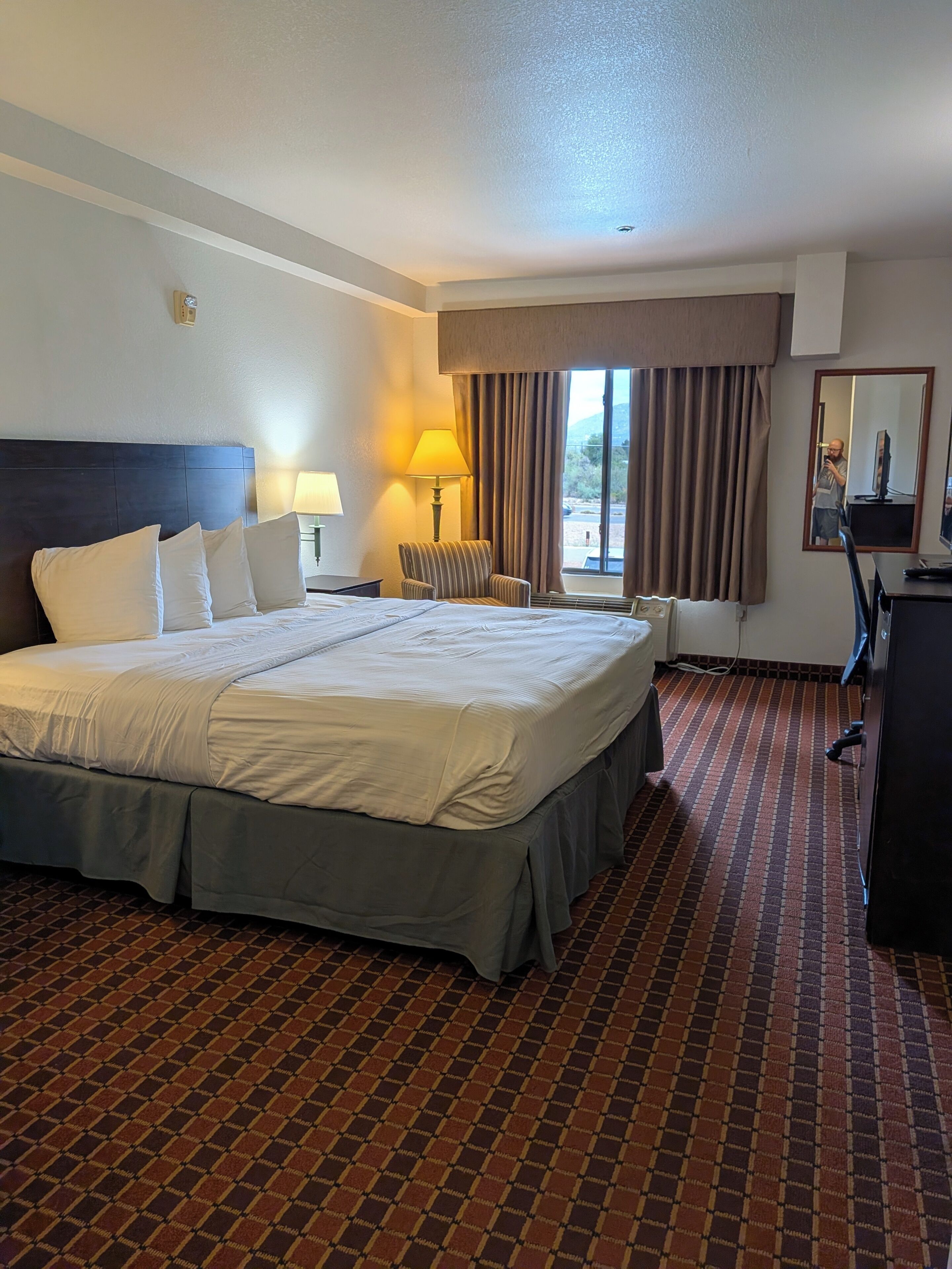 Una habitación de hotel con una cama grande, una silla, un escritorio y una ventana con cortinas.