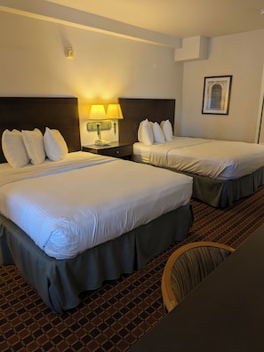 Habitación de hotel con dos camas, una mesita de noche con lámpara, un cuadro enmarcado en la pared y una alfombra estampada.