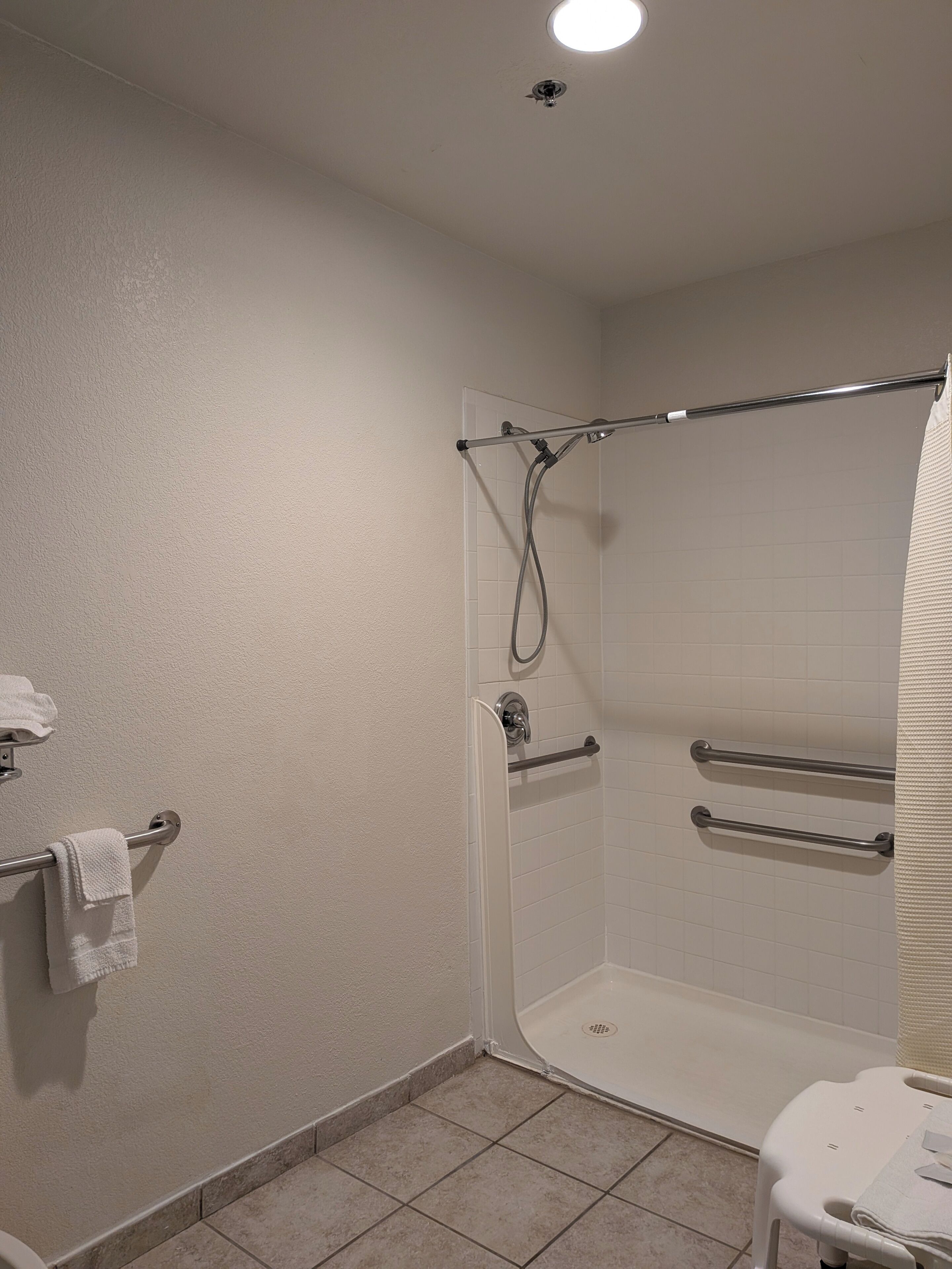 A bathroom with a shower, grab bars, a towel rack, and a toilet.