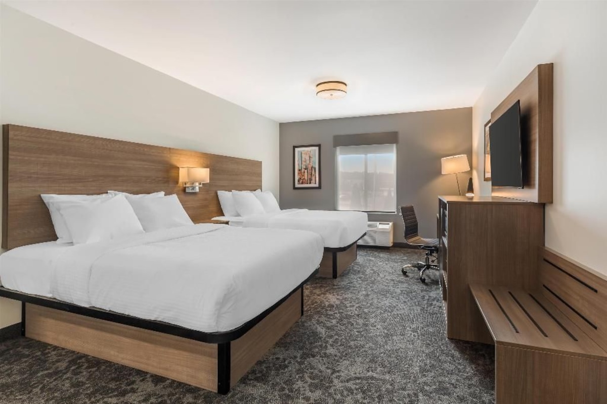 A hotel room with two beds, a desk, a TV, and a large window.