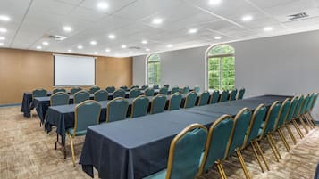 Un salón de conferencias con mesas largas, sillas color turquesa y una pantalla de proyector.