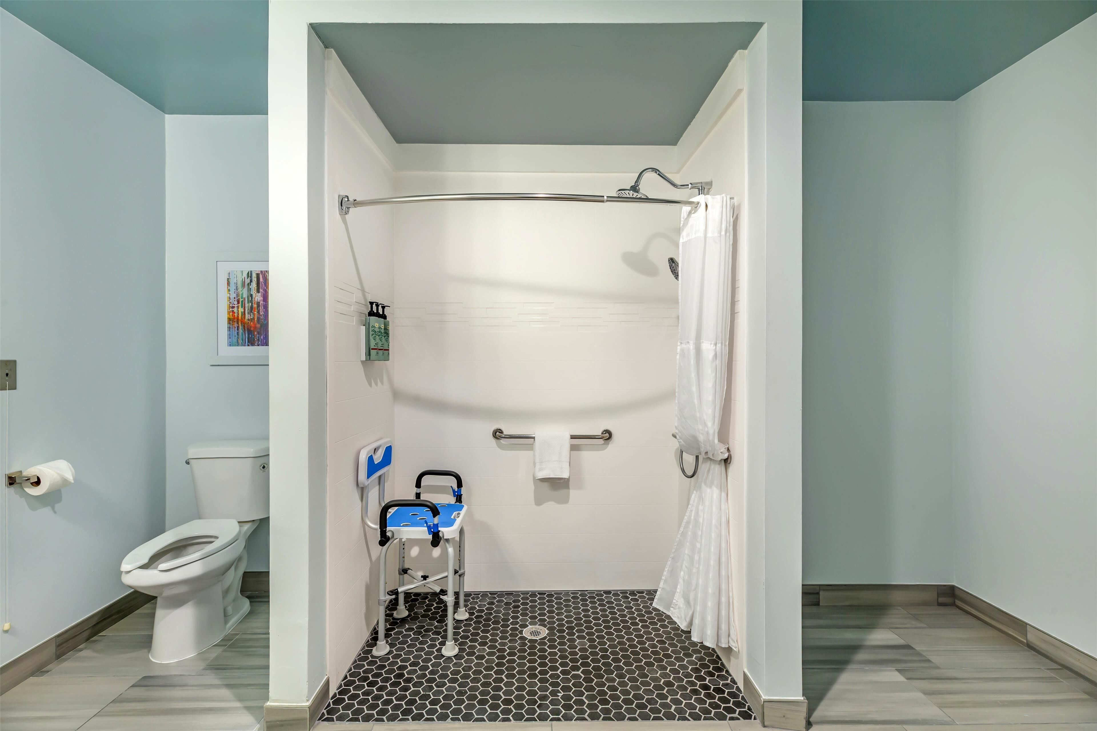 Un baño con ducha, inodoro y un banco accesible para silla de ruedas.