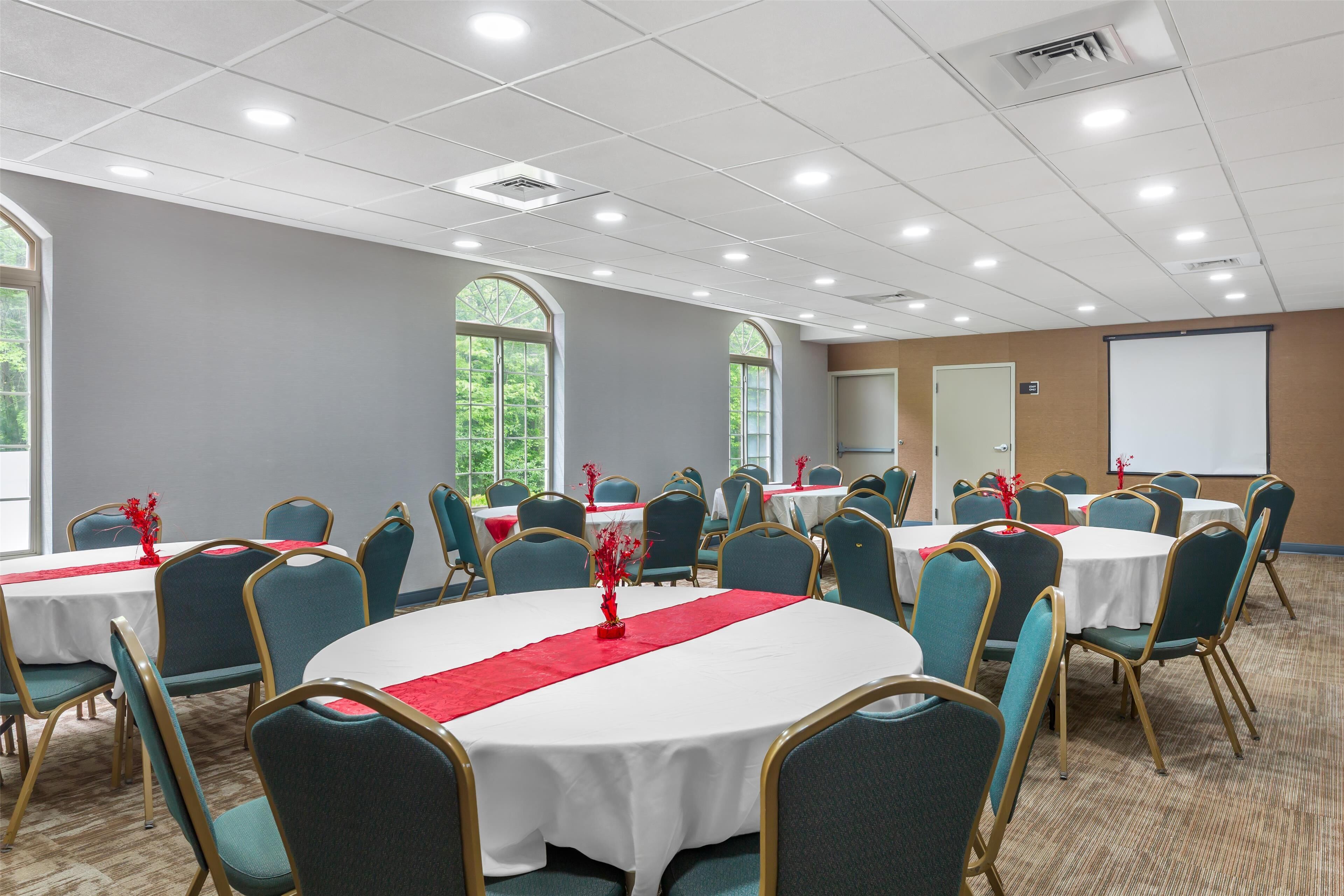 A conference room with round tables, teal chairs, and white tablecloths.