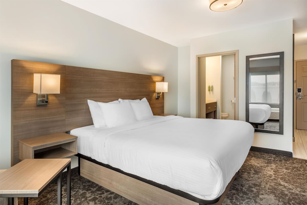 Habitación de hotel con una cama grande, mesitas de noche, un espejo y vistas al exterior.