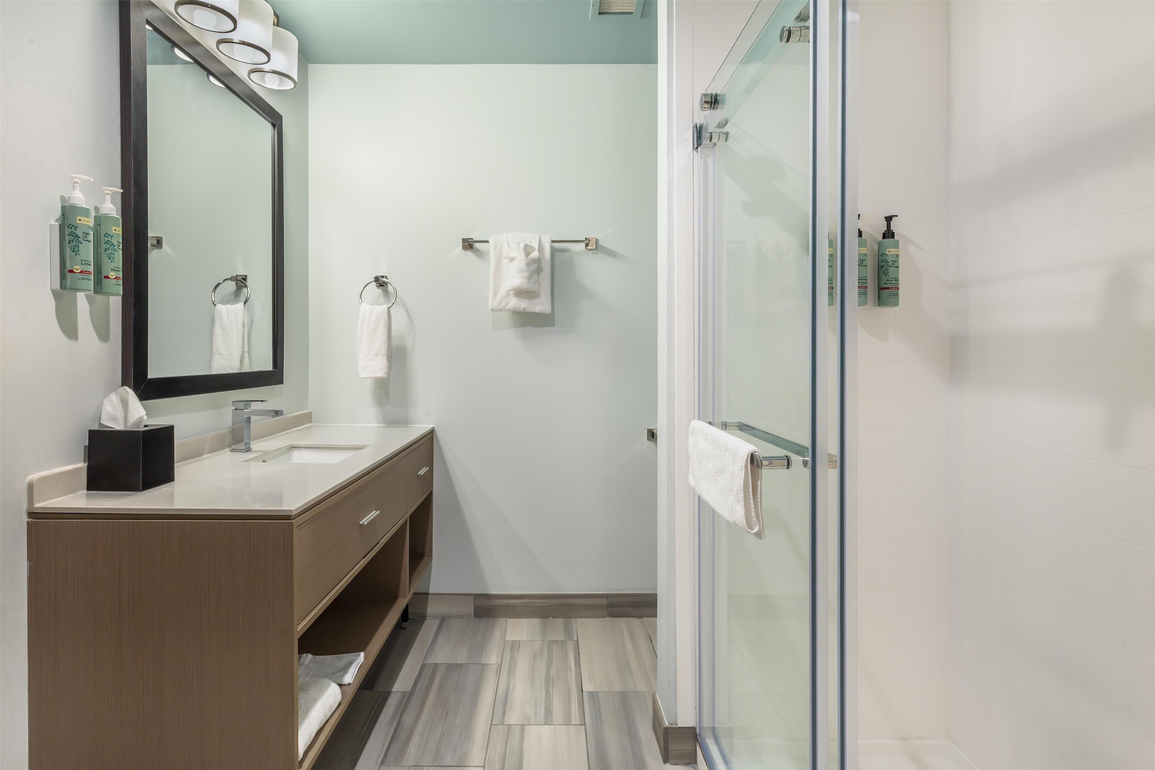 Un baño moderno con tocador de madera, un espejo grande y cabina de ducha de vidrio.