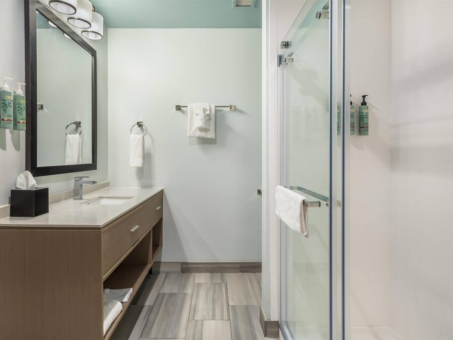 A modern bathroom with a wooden vanity, a large mirror, and a glass shower enclosure.