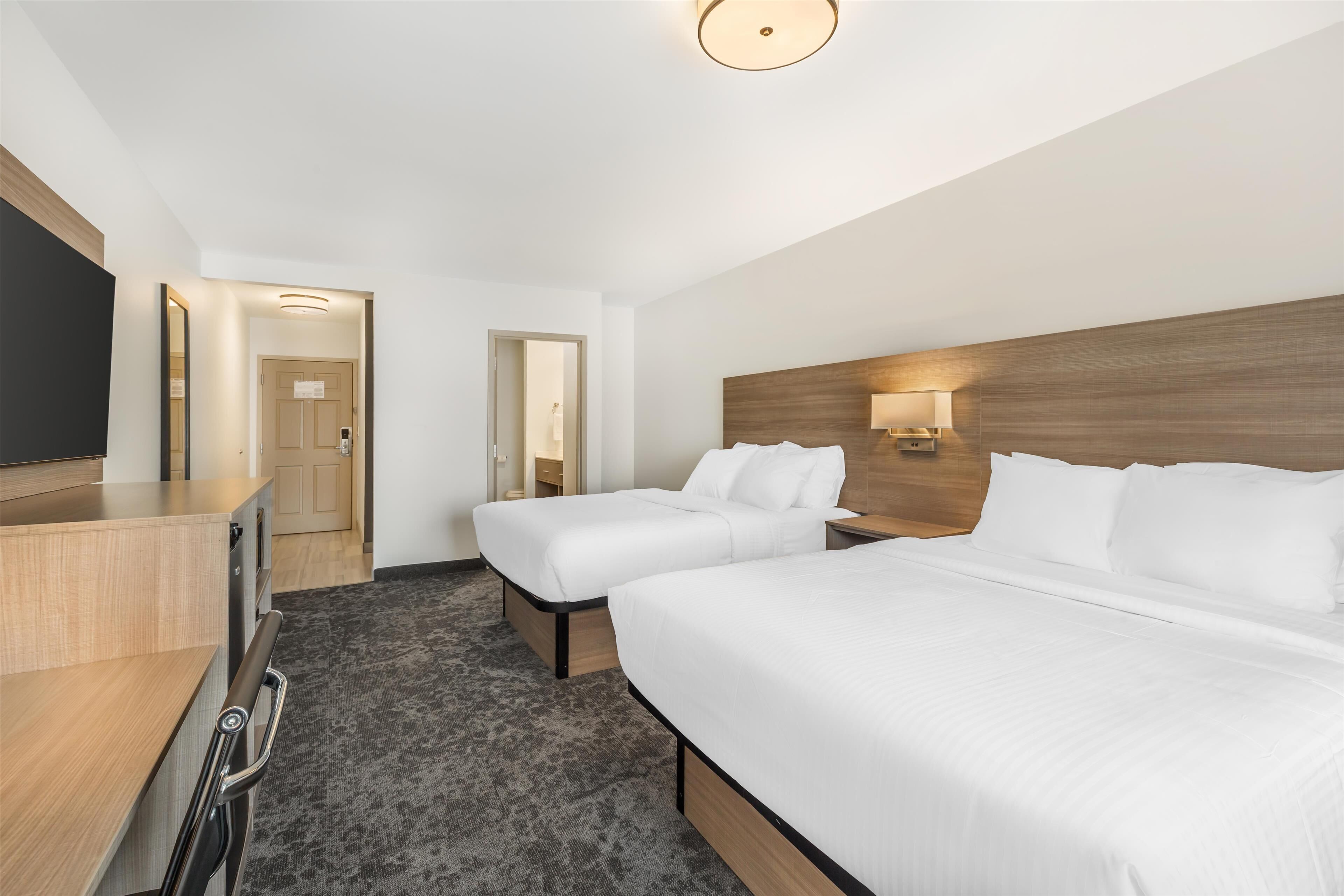 A hotel room with two beds, a desk, and a TV.