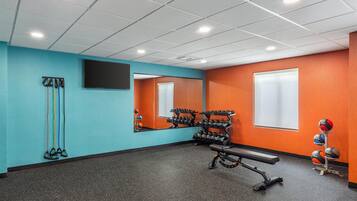 Un gimnasio con pared de espejos, equipamiento de ejercicio y una banca.