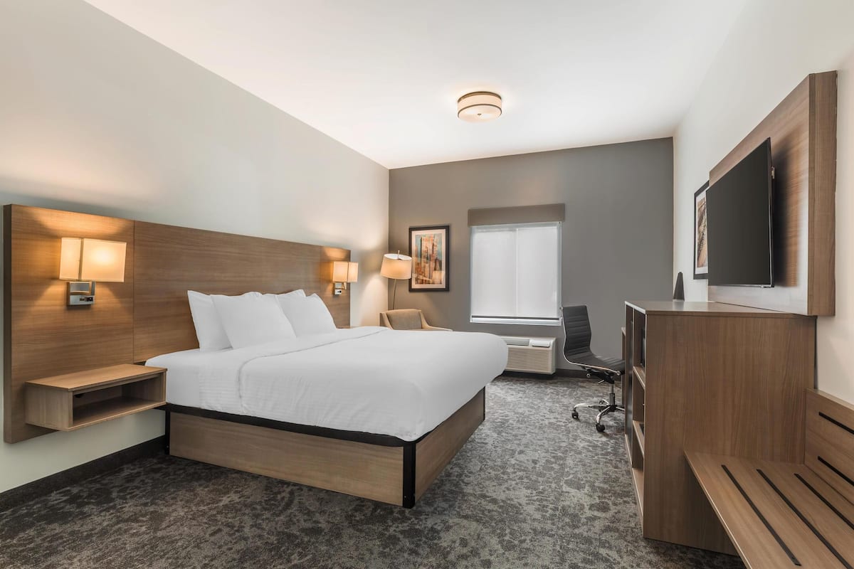 Una habitación de hotel moderna con una cama grande, lámparas de noche, un escritorio, una silla, un televisor y una ventana.
