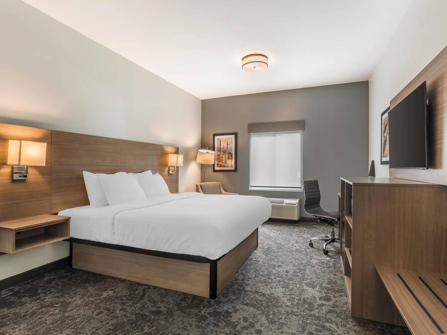 A modern hotel room with a large bed, bedside lamps, a desk, a chair, a TV, and a window.