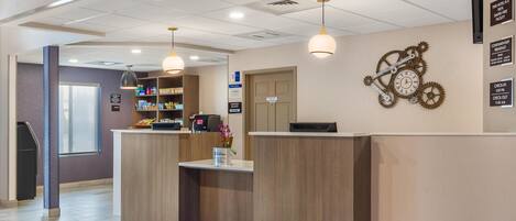 A hotel reception area with a wooden reception desk, a clock with gears on the wall, and a sign indicating check-in and check-out times.
