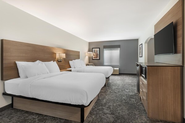A hotel room with two beds, a desk, a flat-screen TV, and a large window.