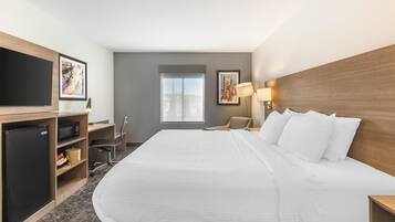 A hotel room with a large bed, a TV, a desk with a chair, a lamp, and a window with a view.