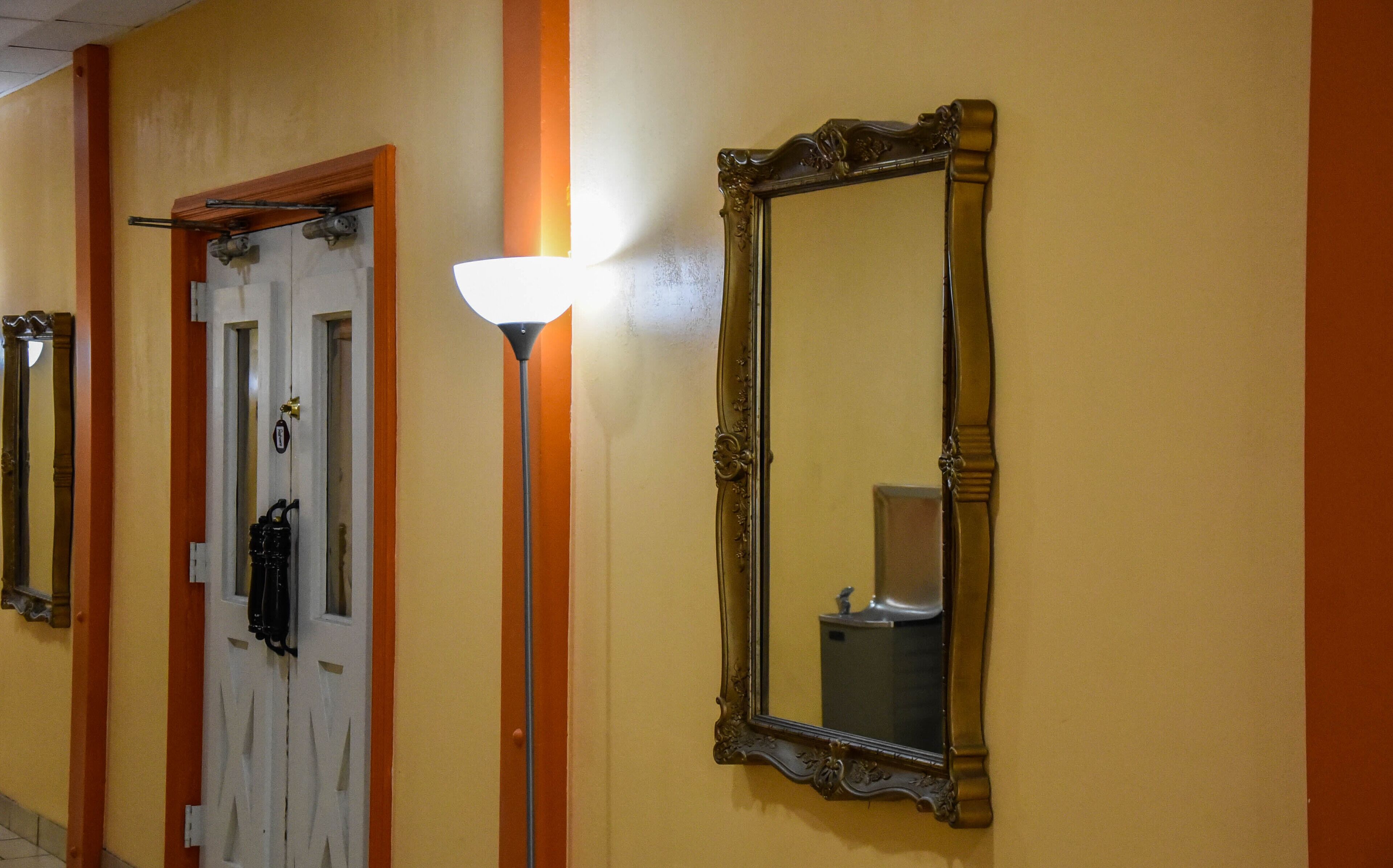 A hallway with a door, a wall-mounted light, and a mirror.