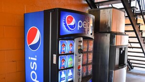 Una máquina expendedora de Pepsi con varias opciones de bebidas, incluyendo gaseosas y agua, frente a un muro de ladrillo.