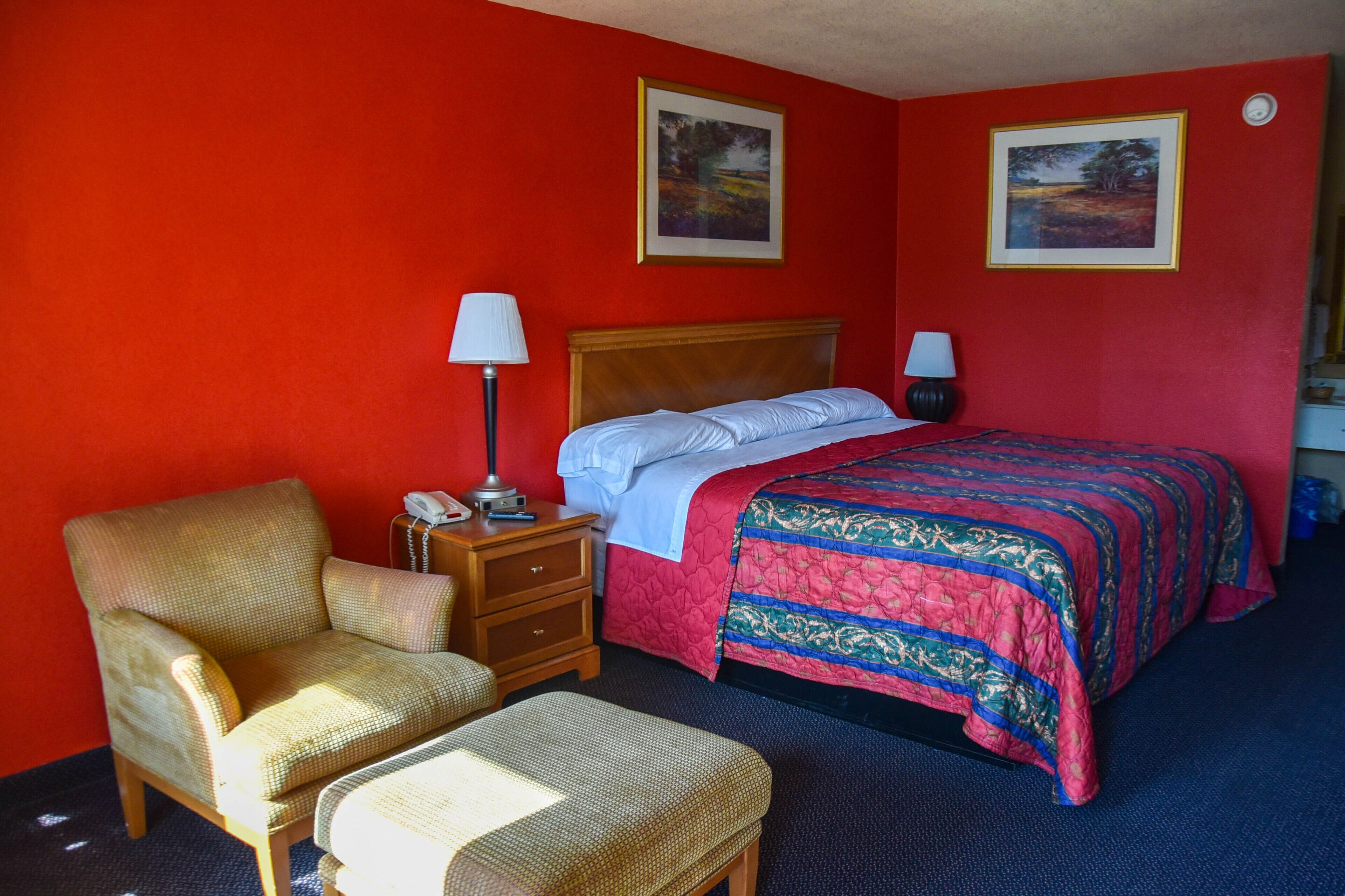 Una habitación de hotel con una cama individual, una silla, una mesita de noche con lámpara y dos cuadros en la pared.