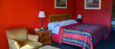 Una habitación de hotel con una cama individual, una silla, una mesita de noche con lámpara y dos cuadros en la pared.