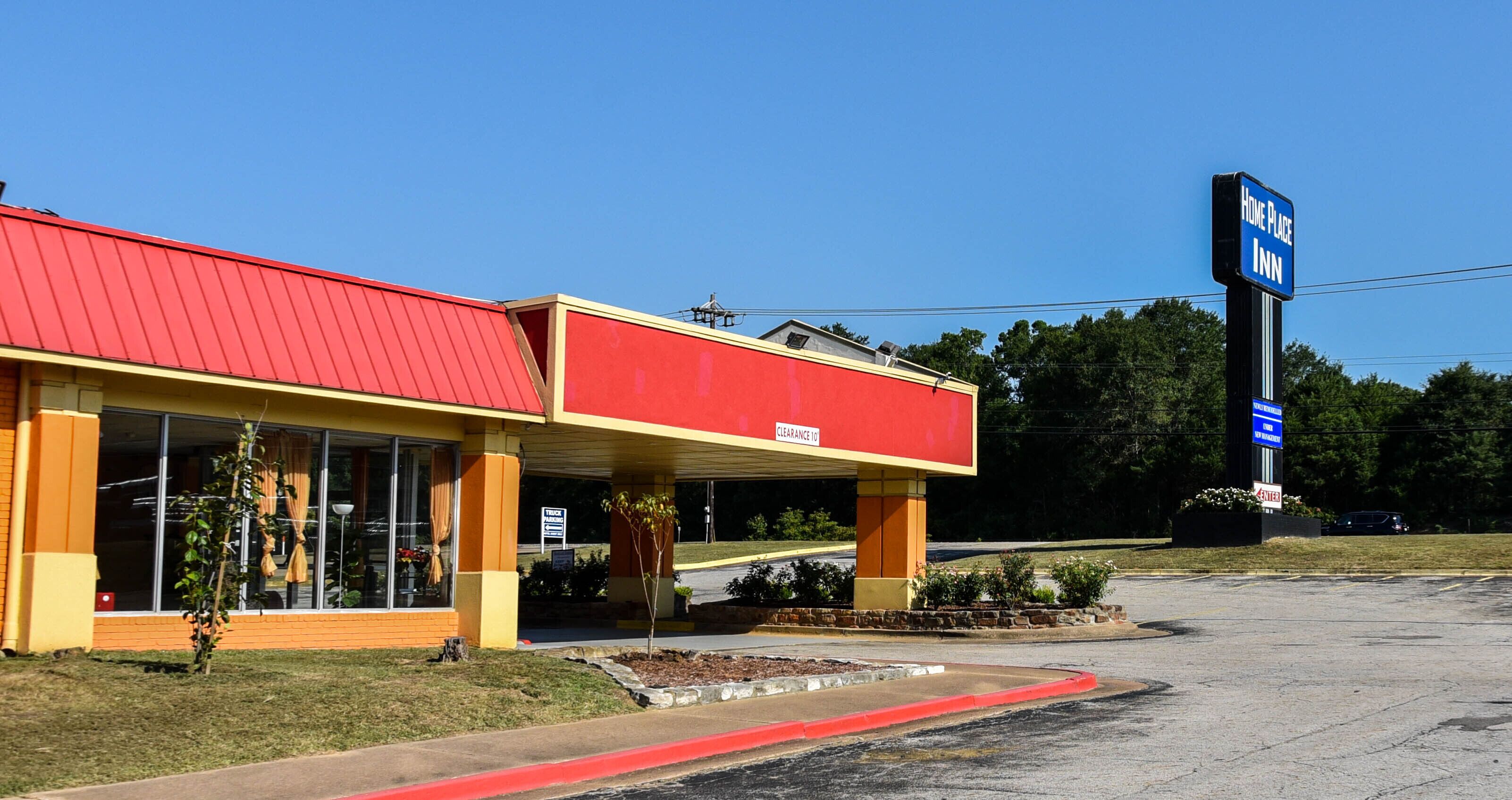 Un hotel con techo rojo y fachada amarilla, con un letrero que indica 'Home Place Inn', y un estacionamiento al frente.
