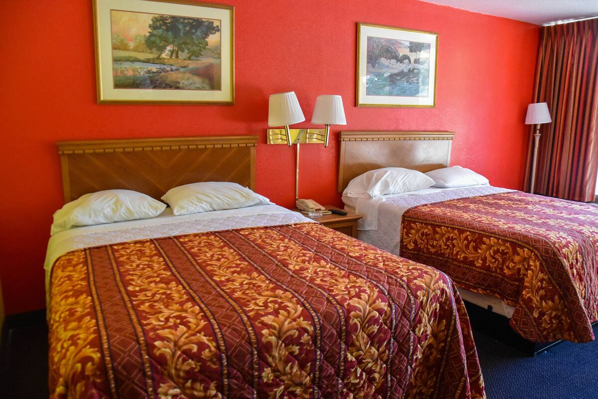 A hotel room with two beds, a wooden headboard, a nightstand, and two wall-mounted lamps.