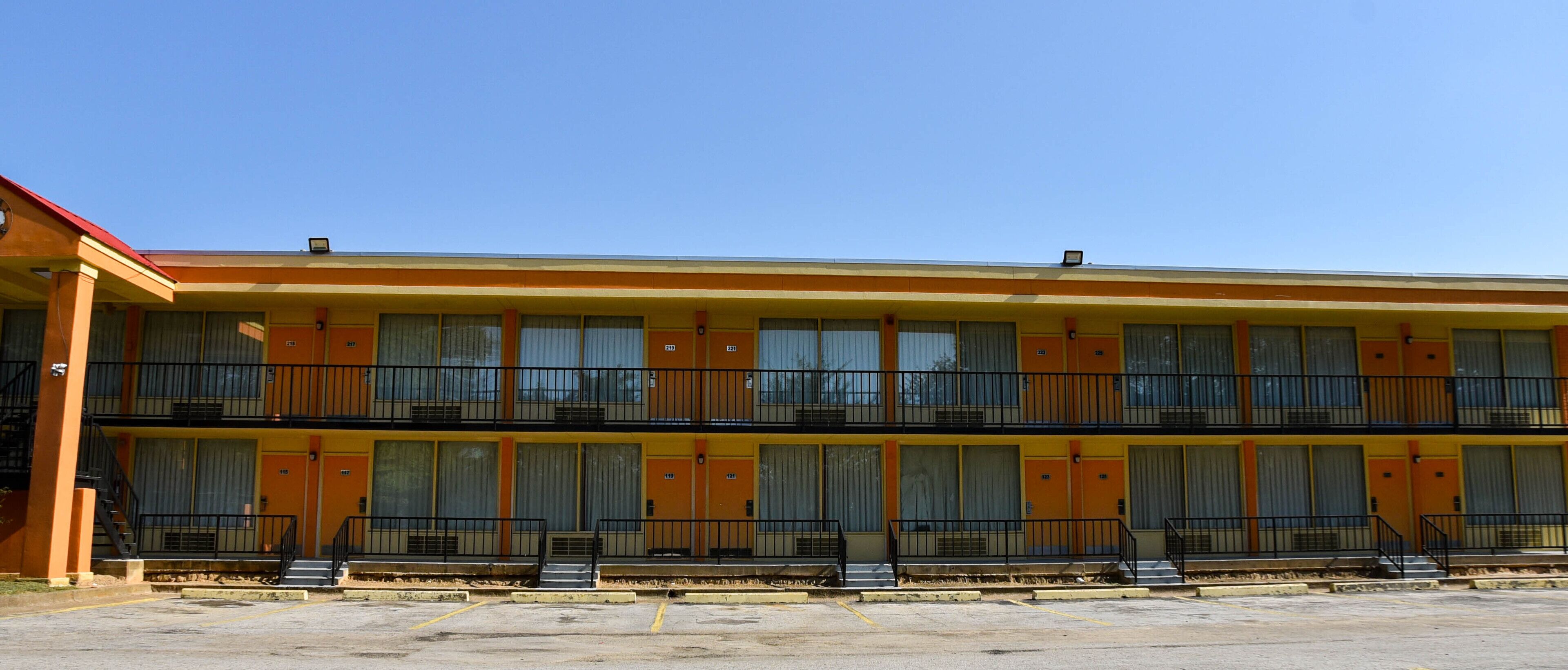 A two-story motel with a flat roof, multiple balconies, and a parking lot in front.