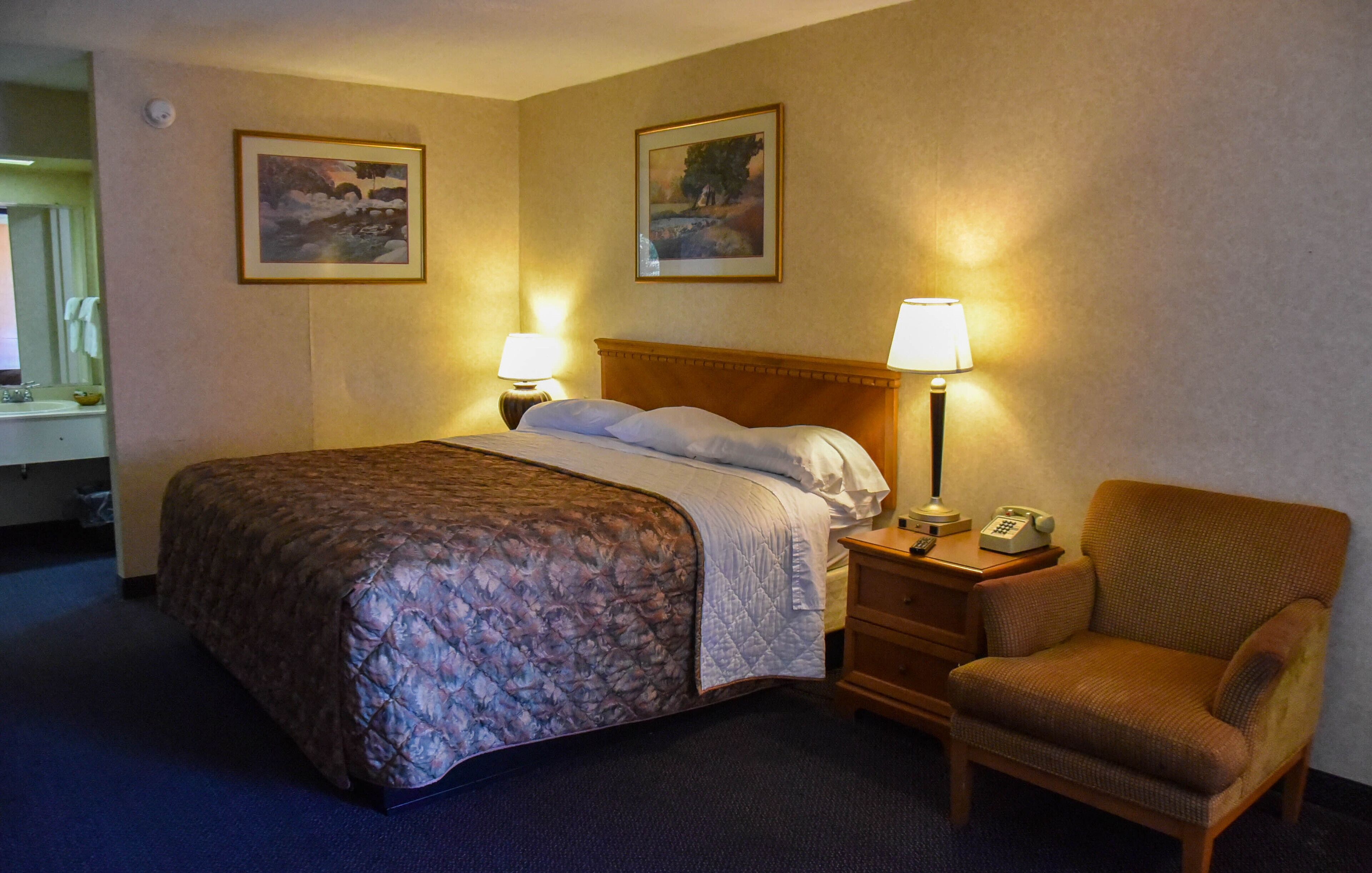 Une chambre d’hôtel avec un lit, deux lampes fixées au mur, une chaise et deux tableaux encadrés accrochés au mur.