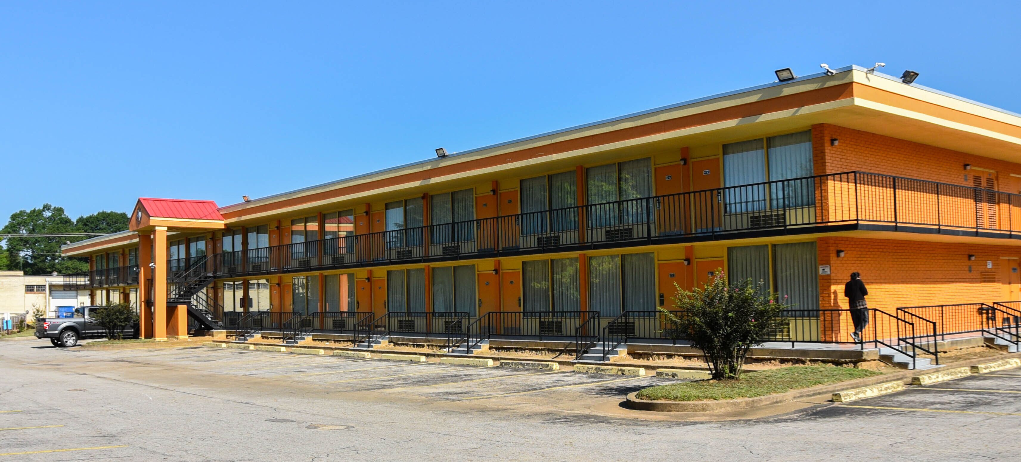 A two-story motel with a red roof, large windows, and a parking lot.