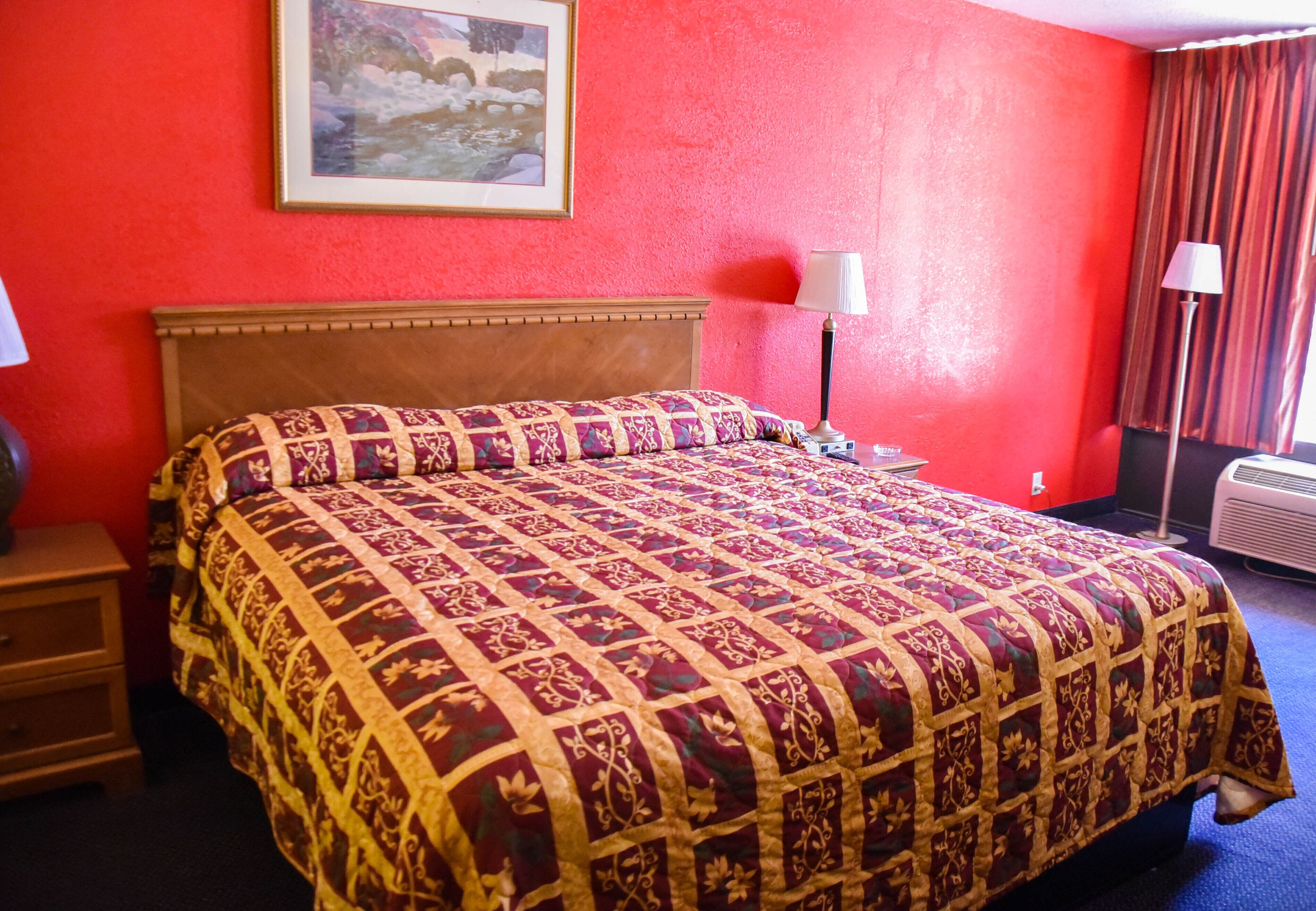 A hotel room with a large bed, a nightstand, a lamp, a painting on the wall, and a window with curtains.