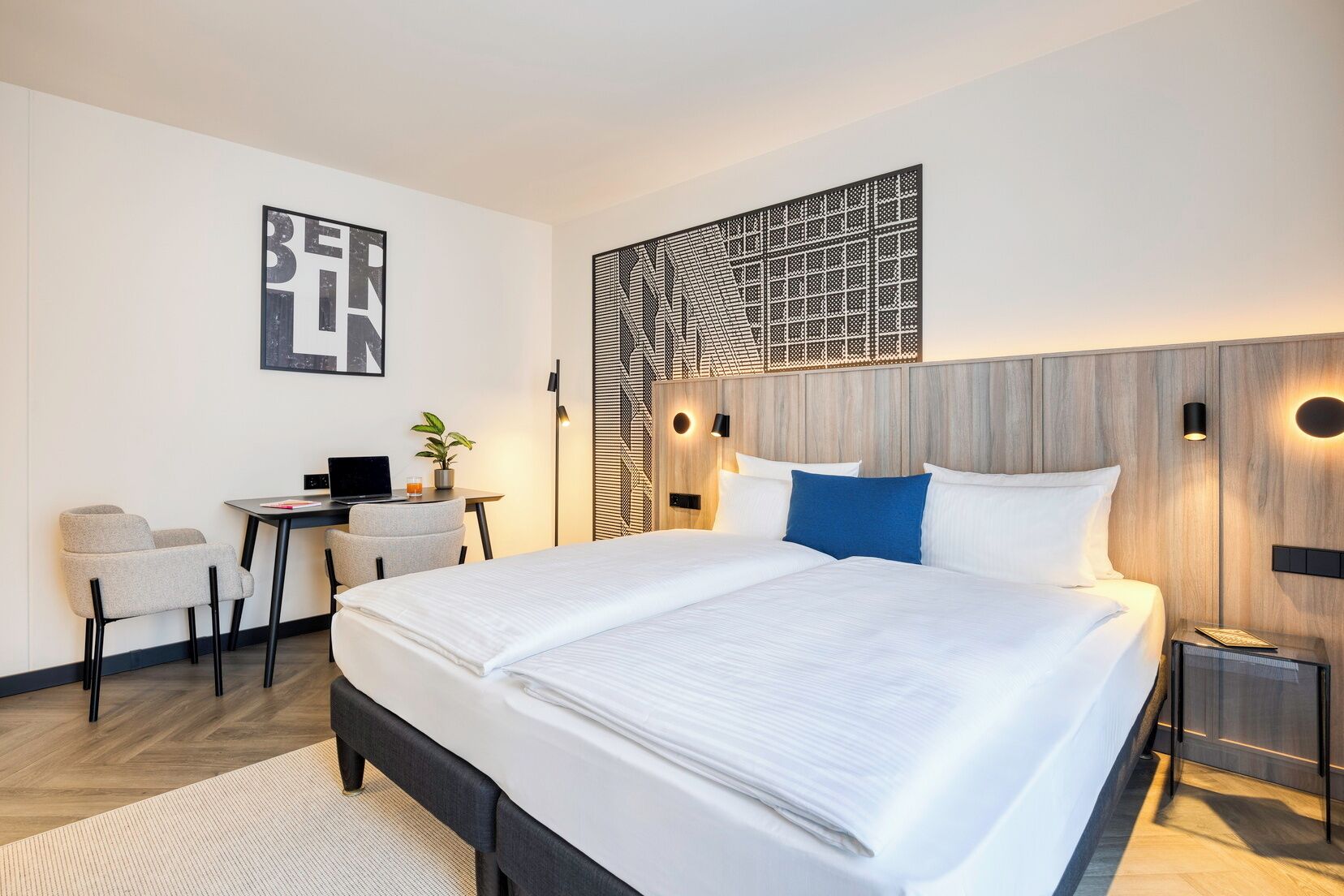 Ett modernt hotellrum med en stor säng, ett skrivbord med en bärbar dator och en stol.