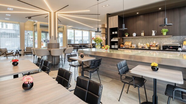 A modern restaurant with a central bar, multiple seating areas, and a kitchen visible in the background. - Citadines Kurfürstendamm Berlin (Berlin)