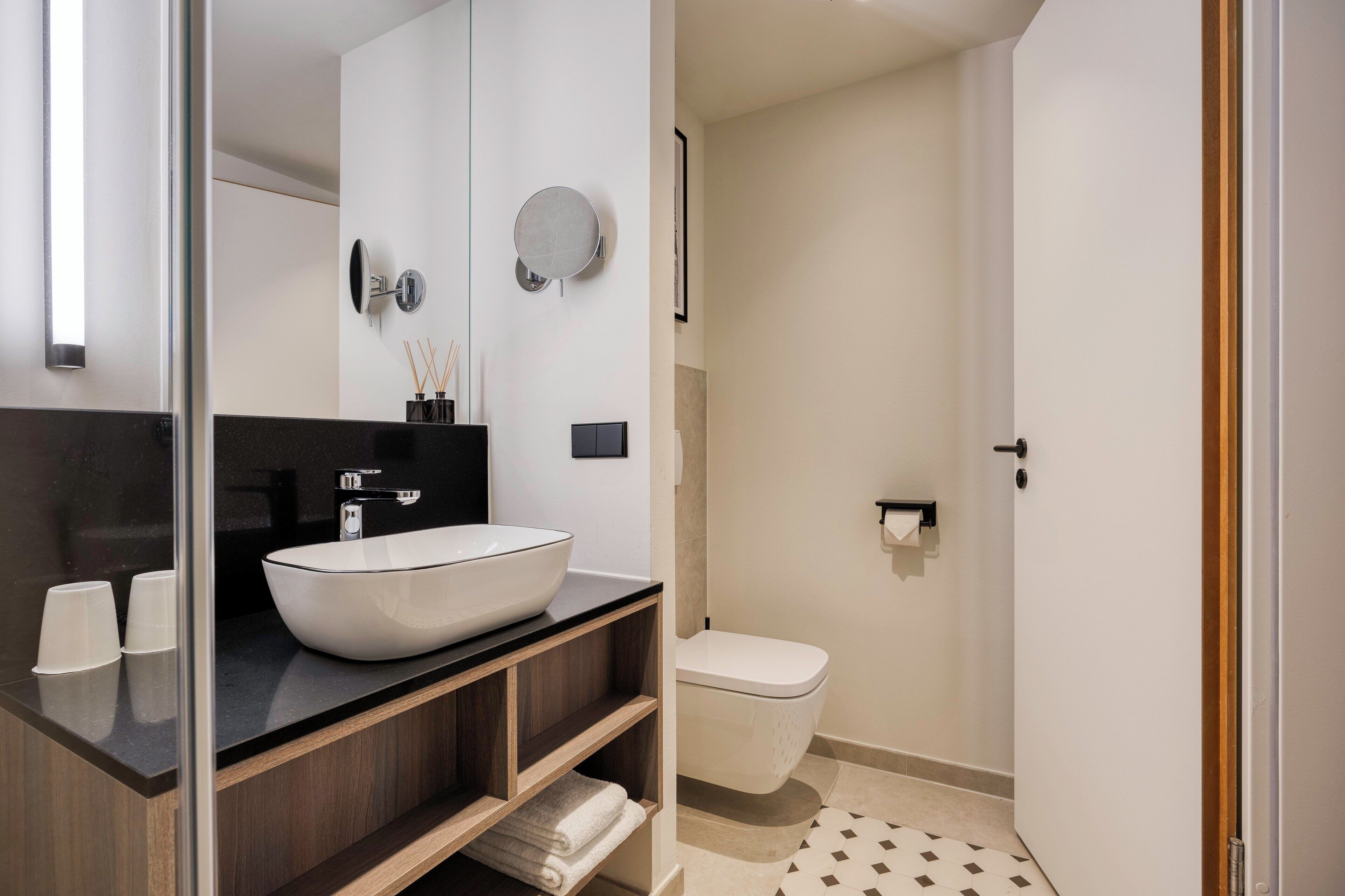 Un baño moderno con un lavamanos grande de color blanco, encimera oscura y un inodoro.