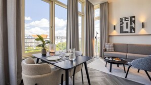 A modern living room with a dining area, large windows, a sofa, and a coffee table. - Citadines Kurfürstendamm Berlin (Berlin)