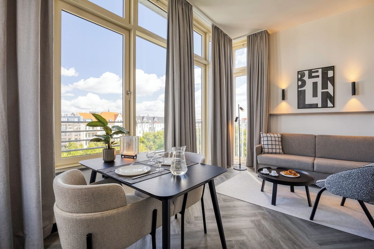 A modern living room with a dining area, large windows, a sofa, and a coffee table.