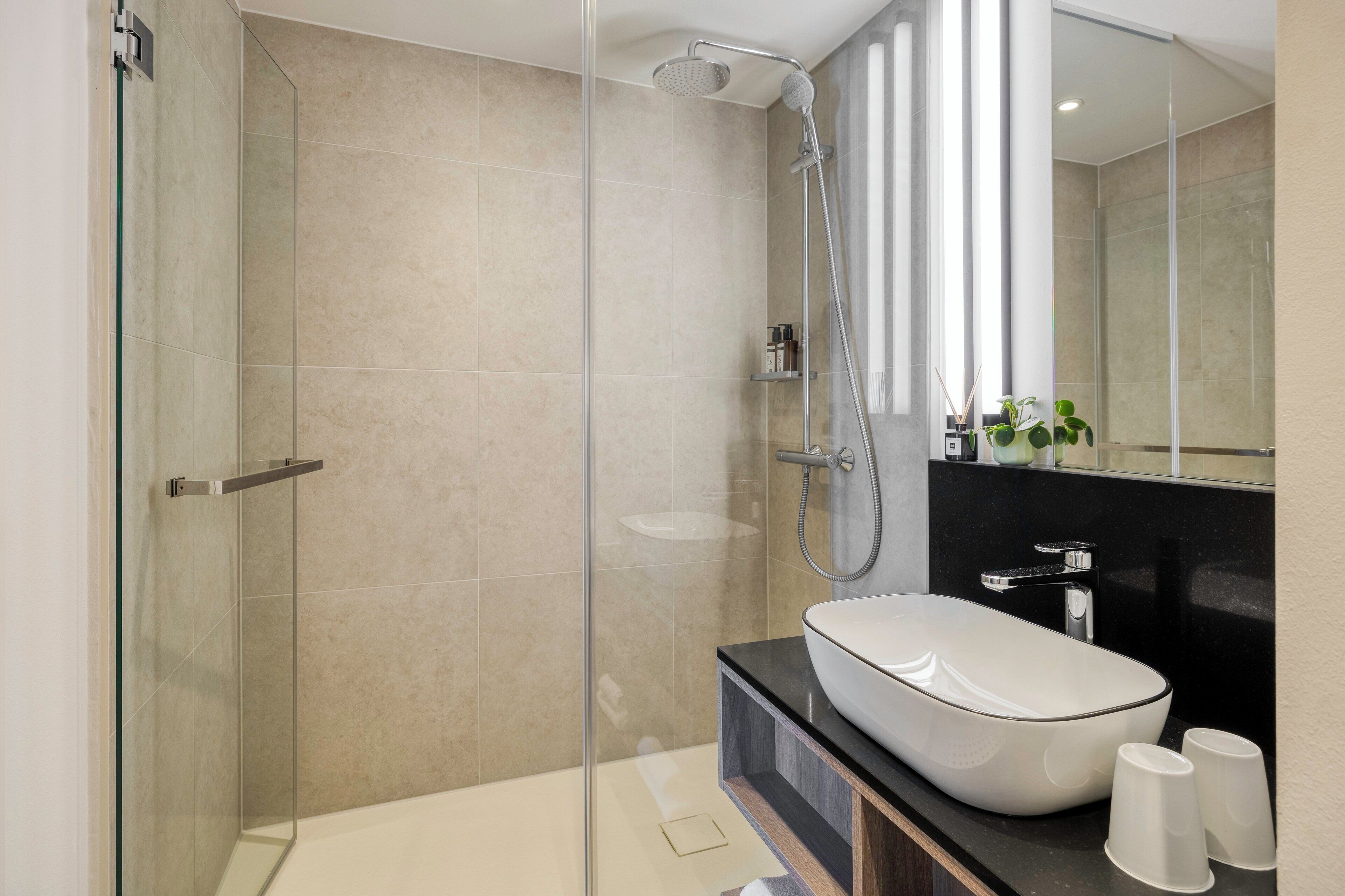 Een moderne badkamer met een douchecabine van glas, een wit wastafeltje en een zwart aanrecht.